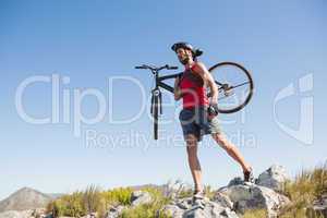 Fit cyclist carrying his bike on rocky terrain