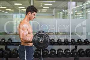 Shirtless muscular man lifting barbell in gym