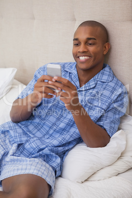 Happy man sitting on bed sending text