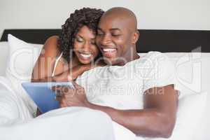 Happy couple using tablet in bed