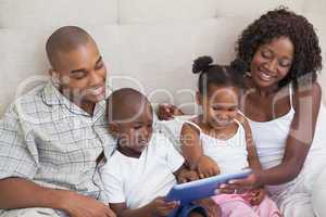 Happy family lying on bed using tablet pc