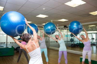 Fitness class holding up exercise balls in studio