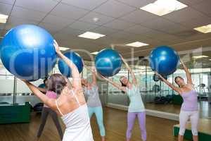 Fitness class holding up exercise balls in studio