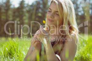 Pretty blonde in sundress sitting on grass holding yellow flower