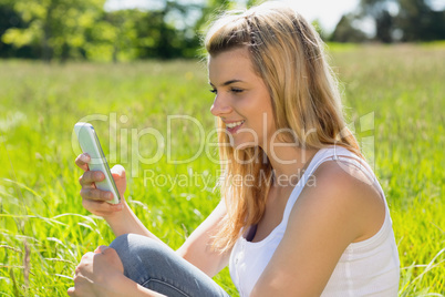 Pretty blonde sitting on grass sending a text
