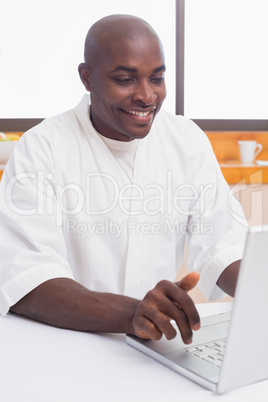 Happy man in bathrobe using laptop at table