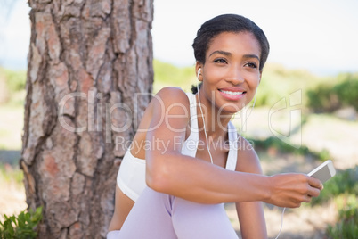 Fit woman sitting against tree listening to music