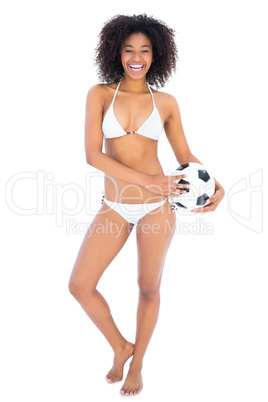 Smiling fit girl in white bikini holding football