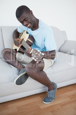 Casual man sitting on sofa playing the guitar