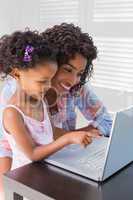 Cute daughter using laptop at desk with mother