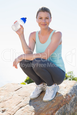 Fit blonde sitting at summit holding water bottle smiling at cam