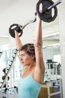 Fit brunette lifting heavy barbell over head