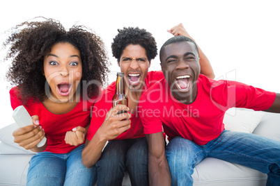 Football fans in red cheering on the sofa with beers