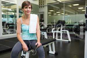 Fit brunette sitting on bench listening to music