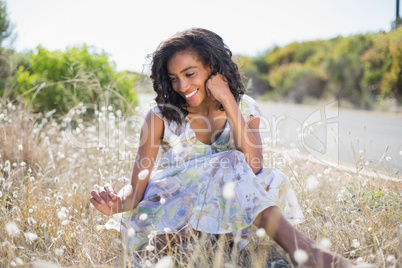 Happy pretty woman sitting on the grass in floral dress