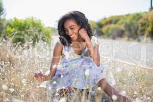 Happy pretty woman sitting on the grass in floral dress
