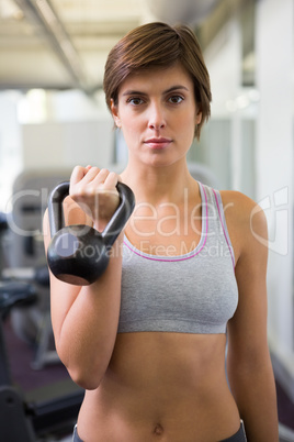 Fit brunette lifting kettlebell looking at camera