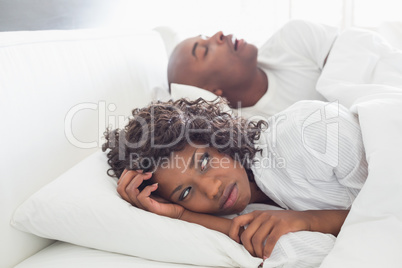 Annoyed woman lying in bed with snoring boyfriend