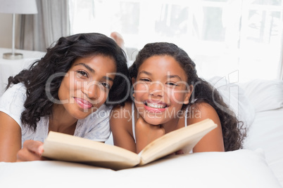 Mother and daughter reading book together on bed