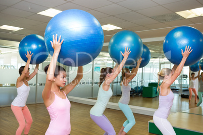 Fitness class holding up exercise balls in studio Fitness class holding up exercise balls in studio