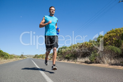 Athletic man jogging on open road holding bottle