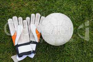 Goalkeeping gloves and football on pitch