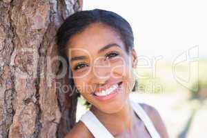 Fit woman leaning against tree smiling at camera