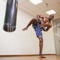 Muscular boxer kicking punching bag in gym