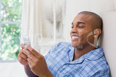 Happy man sitting on bed and texting on phone