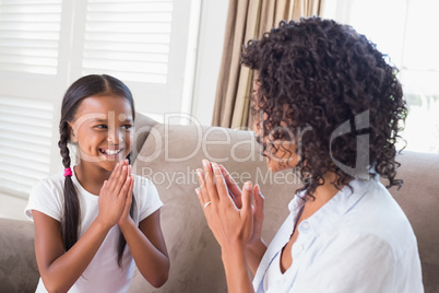 Pretty mother playing clapping game with daughter on couch