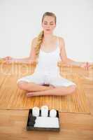 Peaceful blonde sitting in lotus pose on bamboo mat