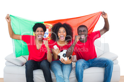 Cheering football fans in red sitting on couch with portugal fla