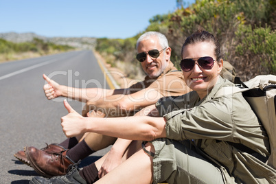 Hitch hiking couple sitting on the side of the road smiling at c