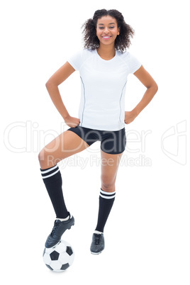 Pretty football player in white holding ball at her foot smiling