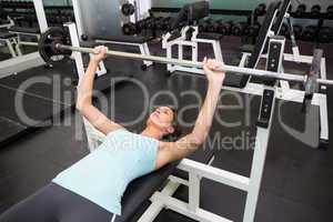 Fit brunette lifting heavy barbell lying on bench