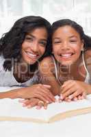 Mother and daughter reading book together on bed
