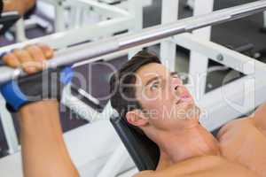 Shirtless muscular man lifting barbell in gym