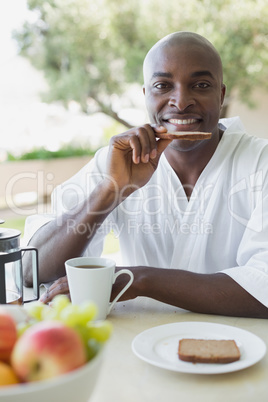 Handsome man in bathrobe having breakfast outside