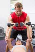 Personal trainer helping client lift dumbbells