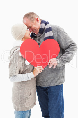 Happy mature couple in winter clothes holding red heart