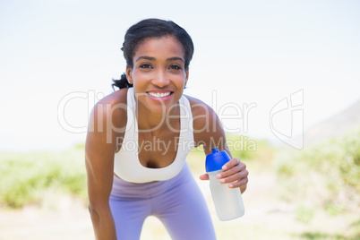 Fit woman holding sports bottle smiling at camera