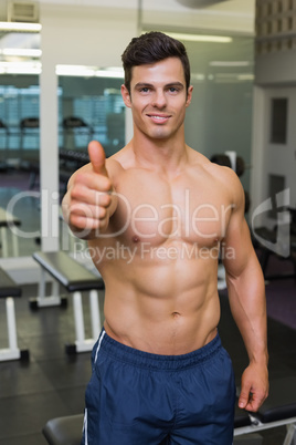 Shirtless muscular man giving thumbs up in gym