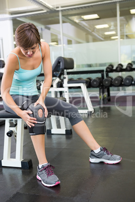 Fit brunette sitting on bench holding injured knee