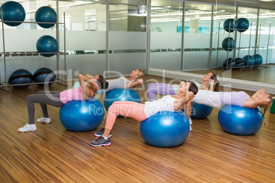 Fitness class doing sit ups on exercise balls in studio