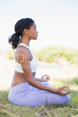 Fit woman sitting on grass in lotus pose with eyes closed