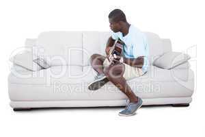 Man sitting on couch learning to play guitar with his tablet pc
