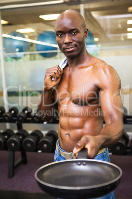 Muscular man holding frying pan in gym