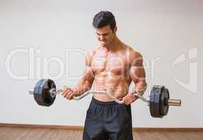 Shirtless muscular man lifting barbell in gym