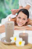 Beautiful brunette enjoying a herbal compress massage smiling at