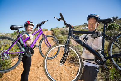 Active couple carrying their bikes on country terrain together